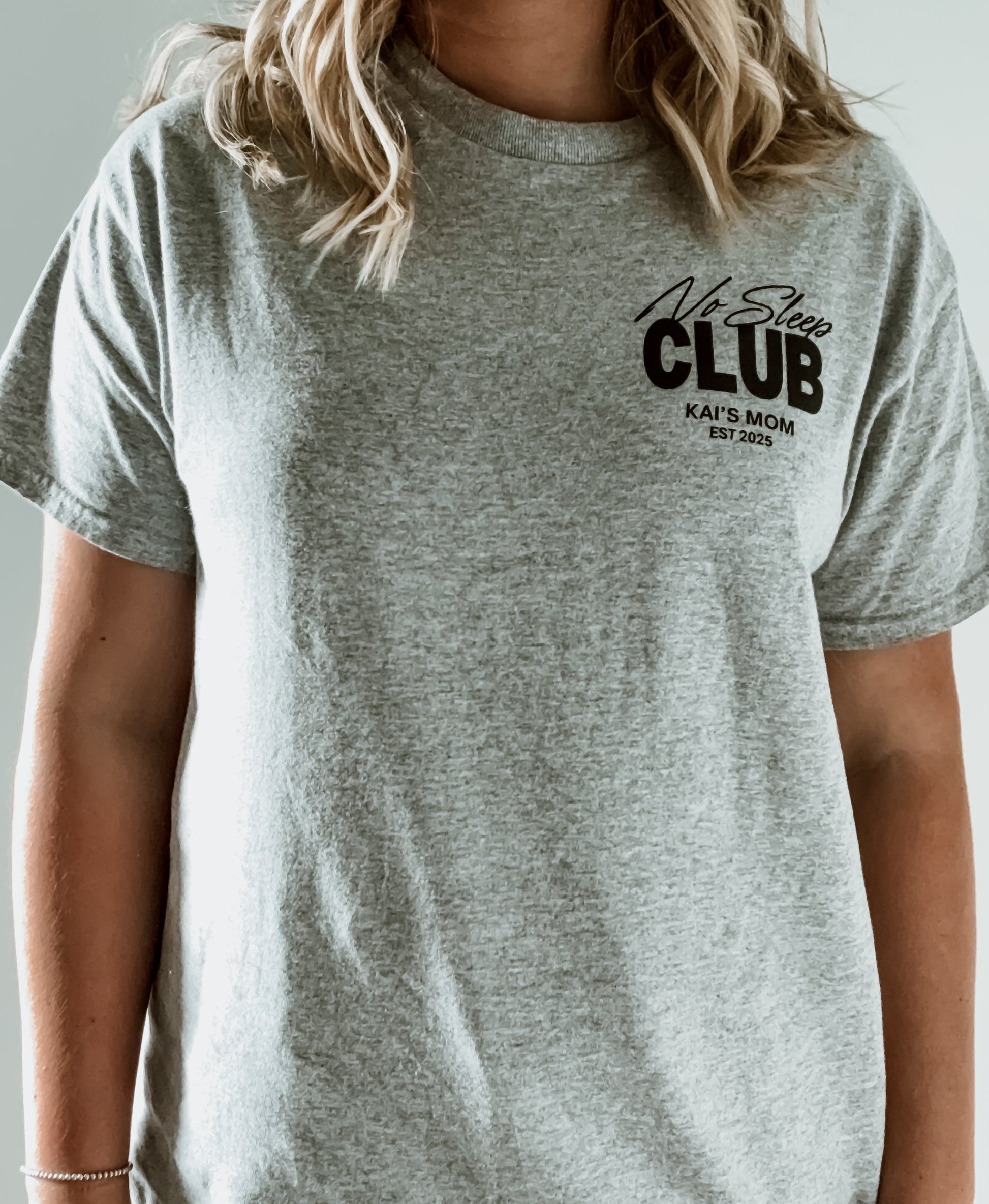 Person wearing a gray t-shirt with 'No Sleep Club' text on a plain background