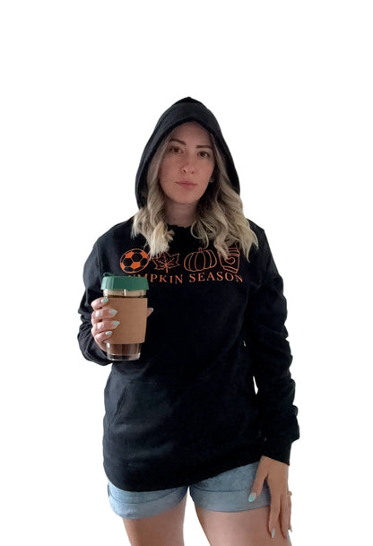 Person wearing a black hoodie with 'Pumpkin Season' text, holding a coffee cup.