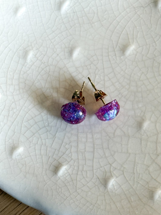 Pair of earrings with purple and pink glittery stones on a textured white surface