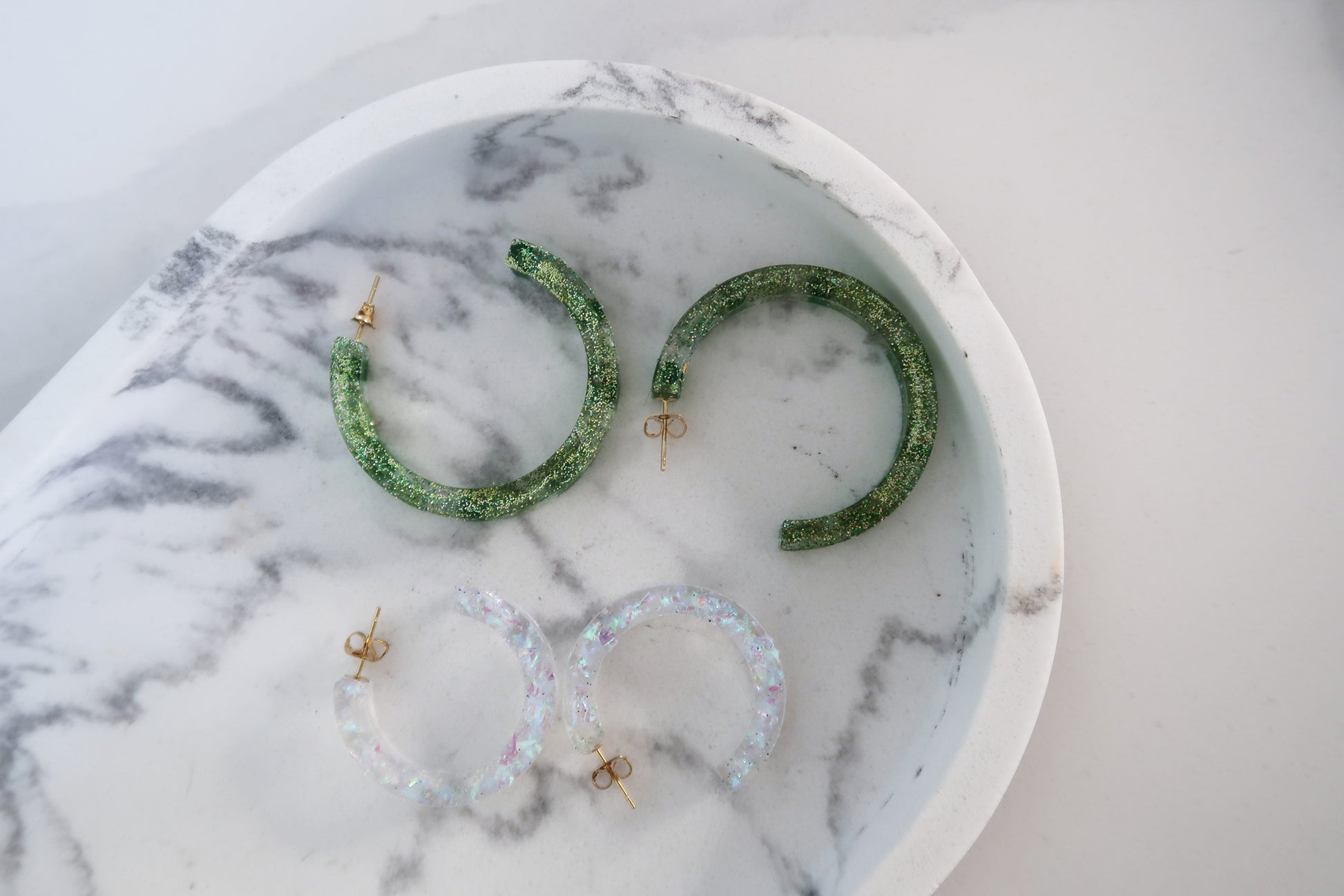 Metallic sparkly green hoop earrings paired with mini clear hoop earrings