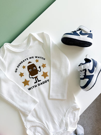 White baby onesie with a printed design and baby shoes on a light surface.