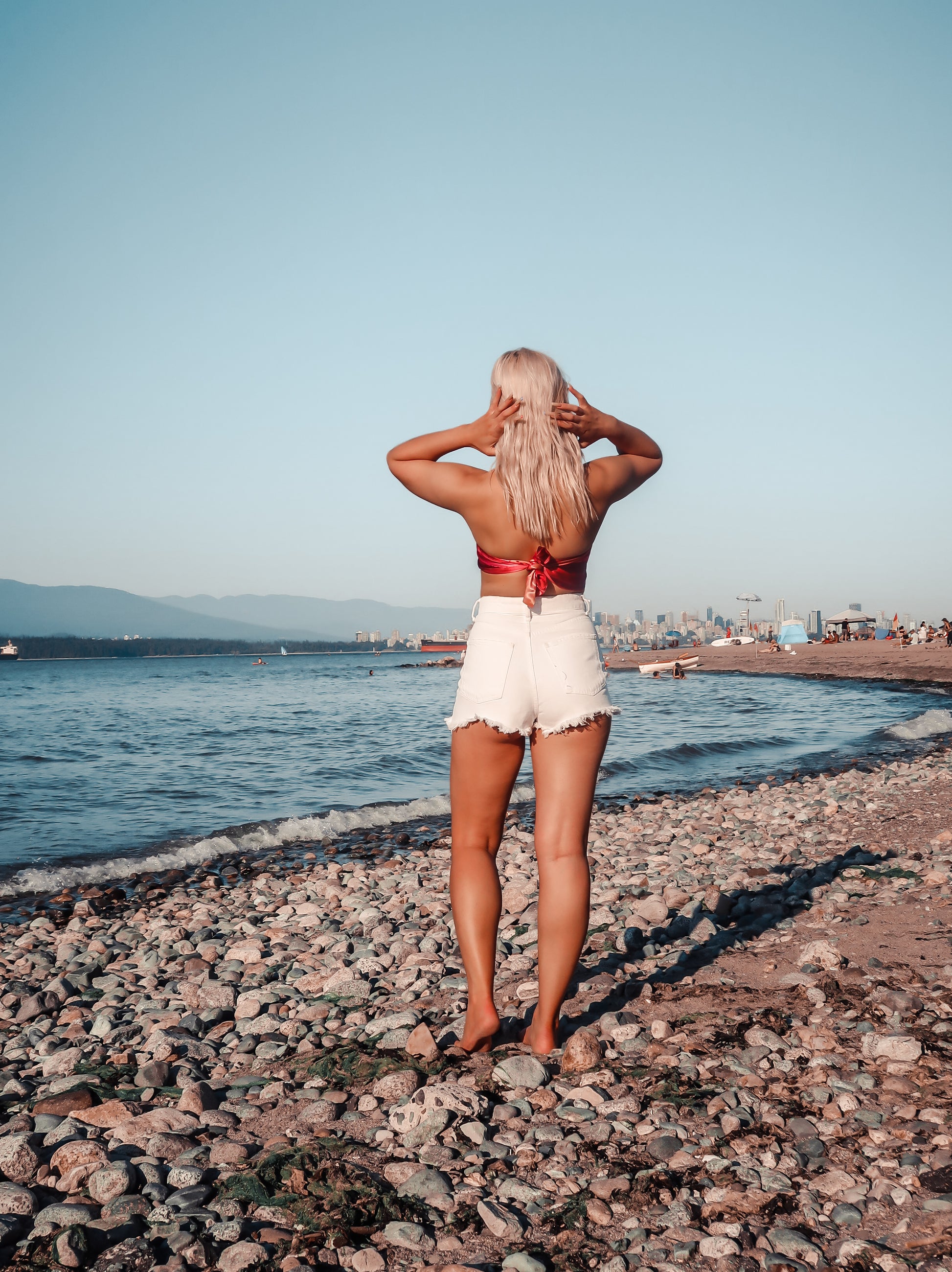 woman standing on rocky beach wearing hot pink and orange bandeau top with white shorts