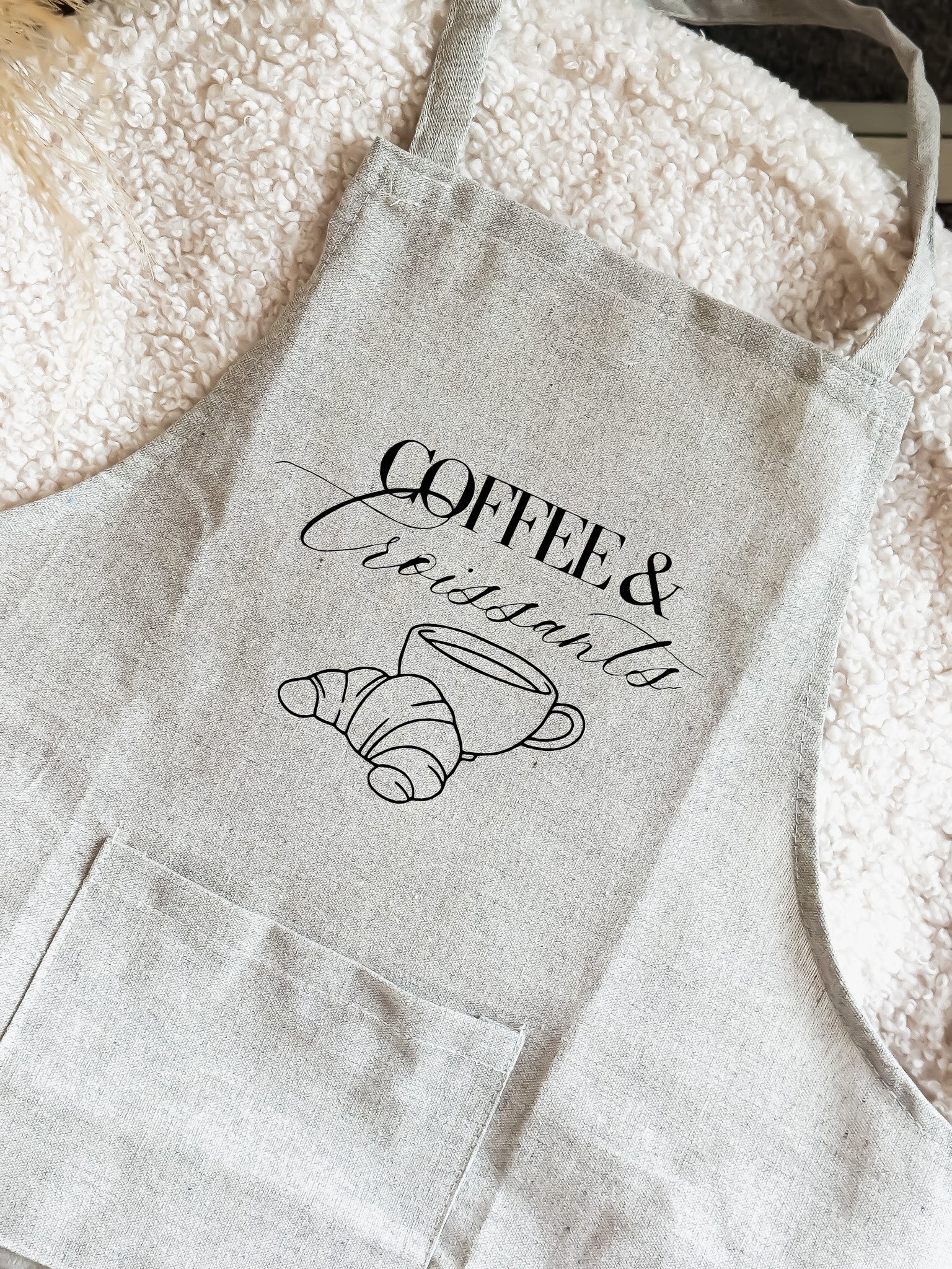 Light gray apron with 'Coffee & Croissants' text and cup illustration on a flour-dusted surface.