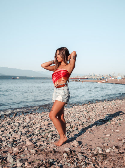 woman standing on beach wearing hot pink and orange silk bandana top and jean shorts