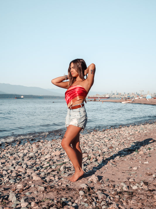 woman standing on beach wearing hot pink and orange silk bandana top and jean shorts