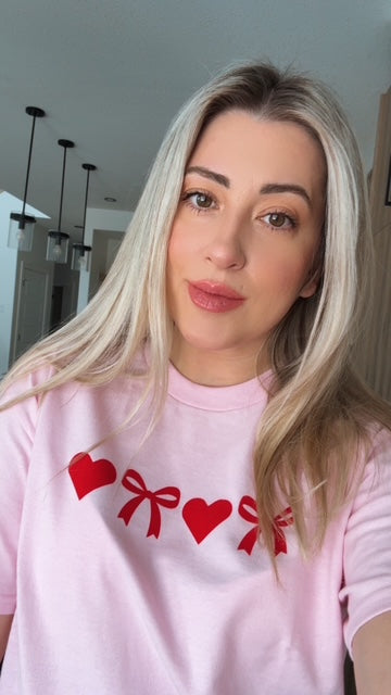 Person wearing a pink sweatshirt with red heart and bow designs indoors.