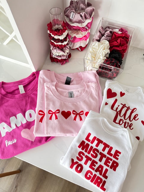 Children's clothing set with t-shirts and shorts on a table, featuring text and hearts.