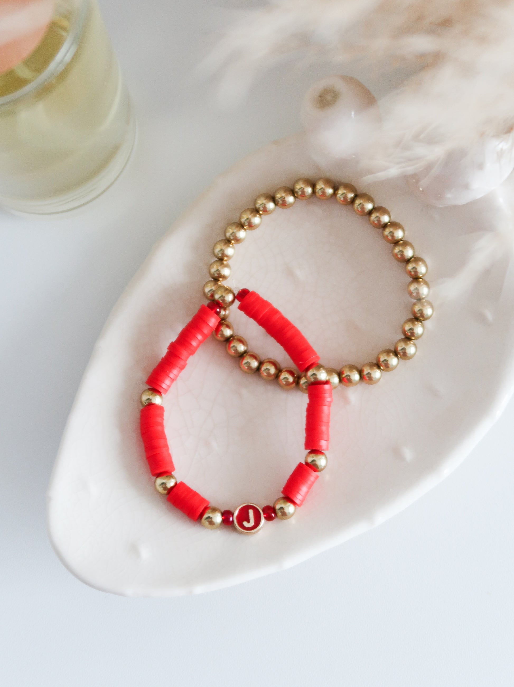 Two beaded bracelets, one red and one gold, on a white surface.