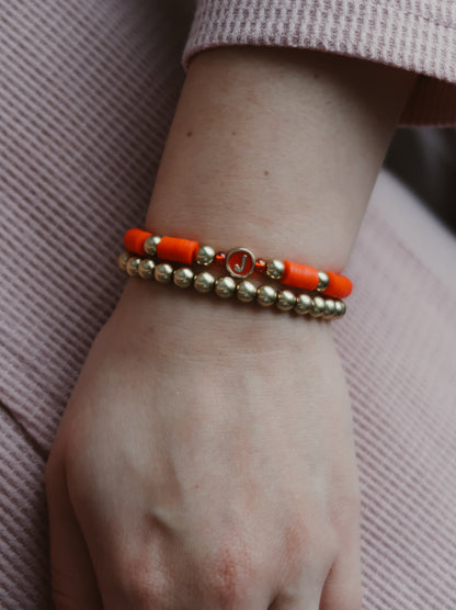 Orange and gold beaded bracelet on a wrist against a pink fabric background