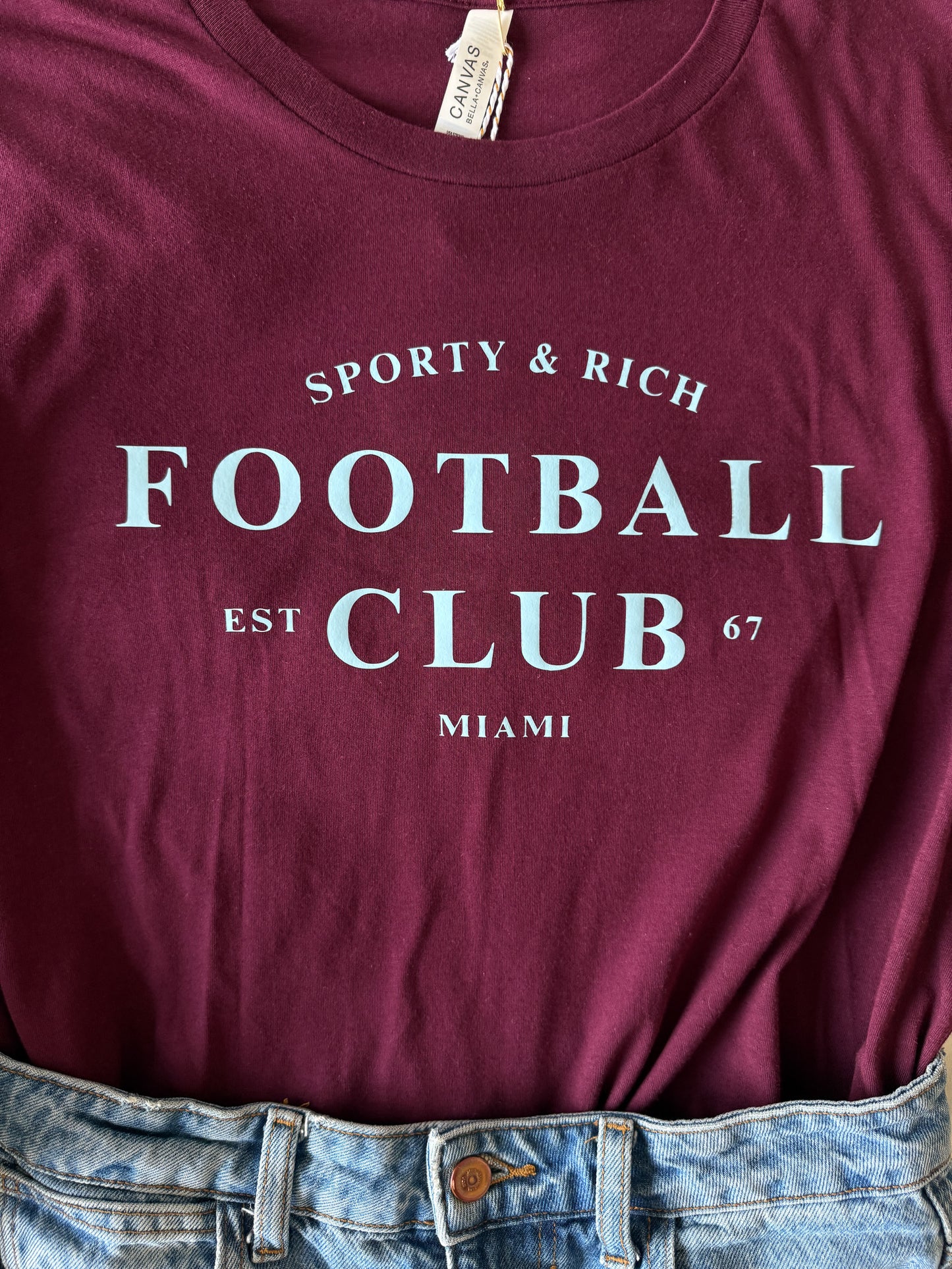 Maroon t-shirt with 'Sporty & Rich Football Club' text on a plain background