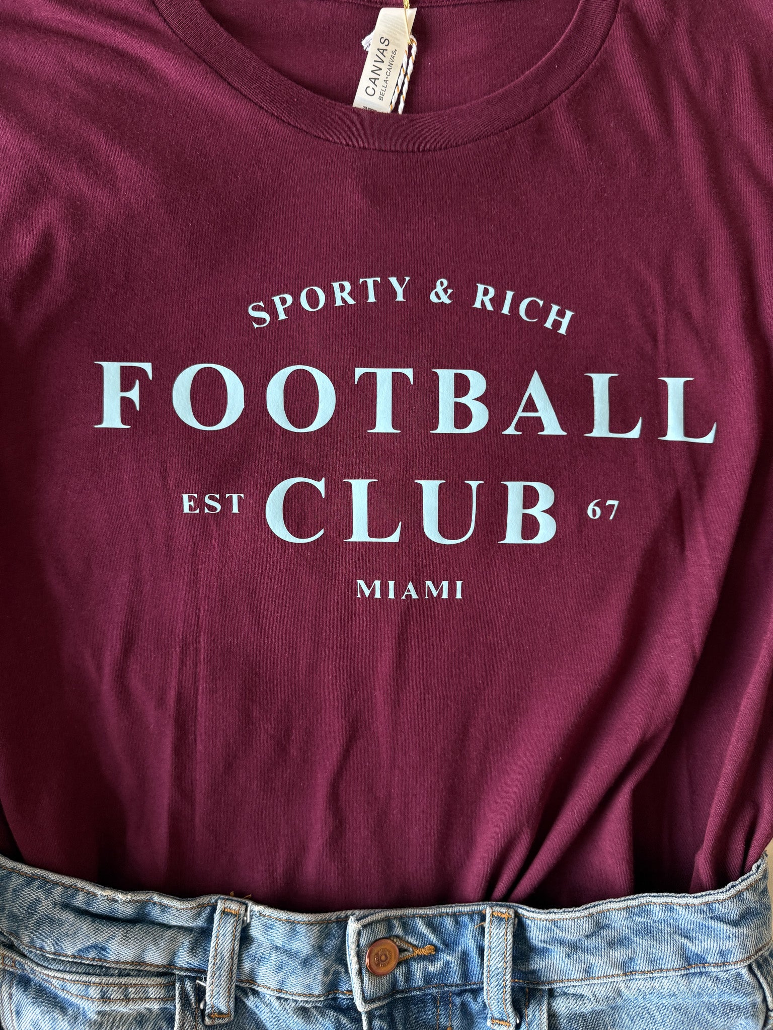 Maroon t-shirt with 'Sporty & Rich Football Club' text on a plain background