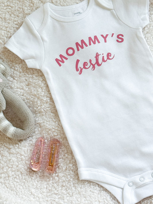 White baby onesie with 'Mommy's bestie' text on a textured surface