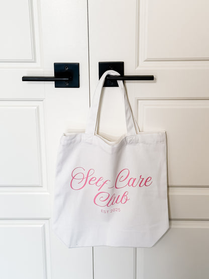 White tote bag with 'Sex Care Club' text hanging on a door handle.