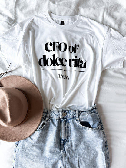 White t-shirt with 'CEO of dolce vita Italia' text, paired with a beige hat and denim shorts on a white background.