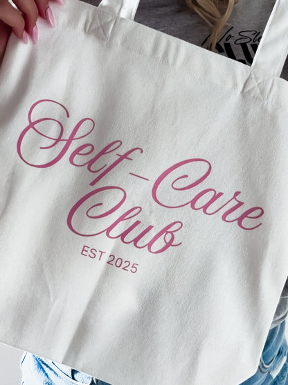 Tote bag with 'Self-Care Club EST 2025' text in pink on a white background