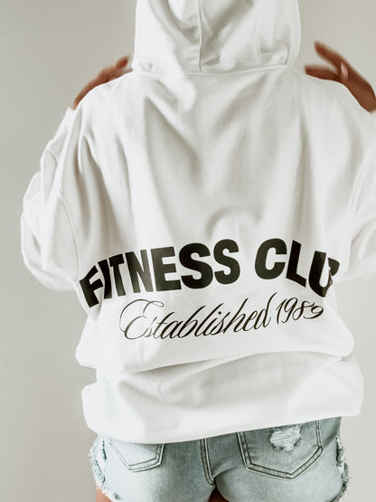 White hoodie with 'Fitness Club Established 1985' text on the back, worn by a person.