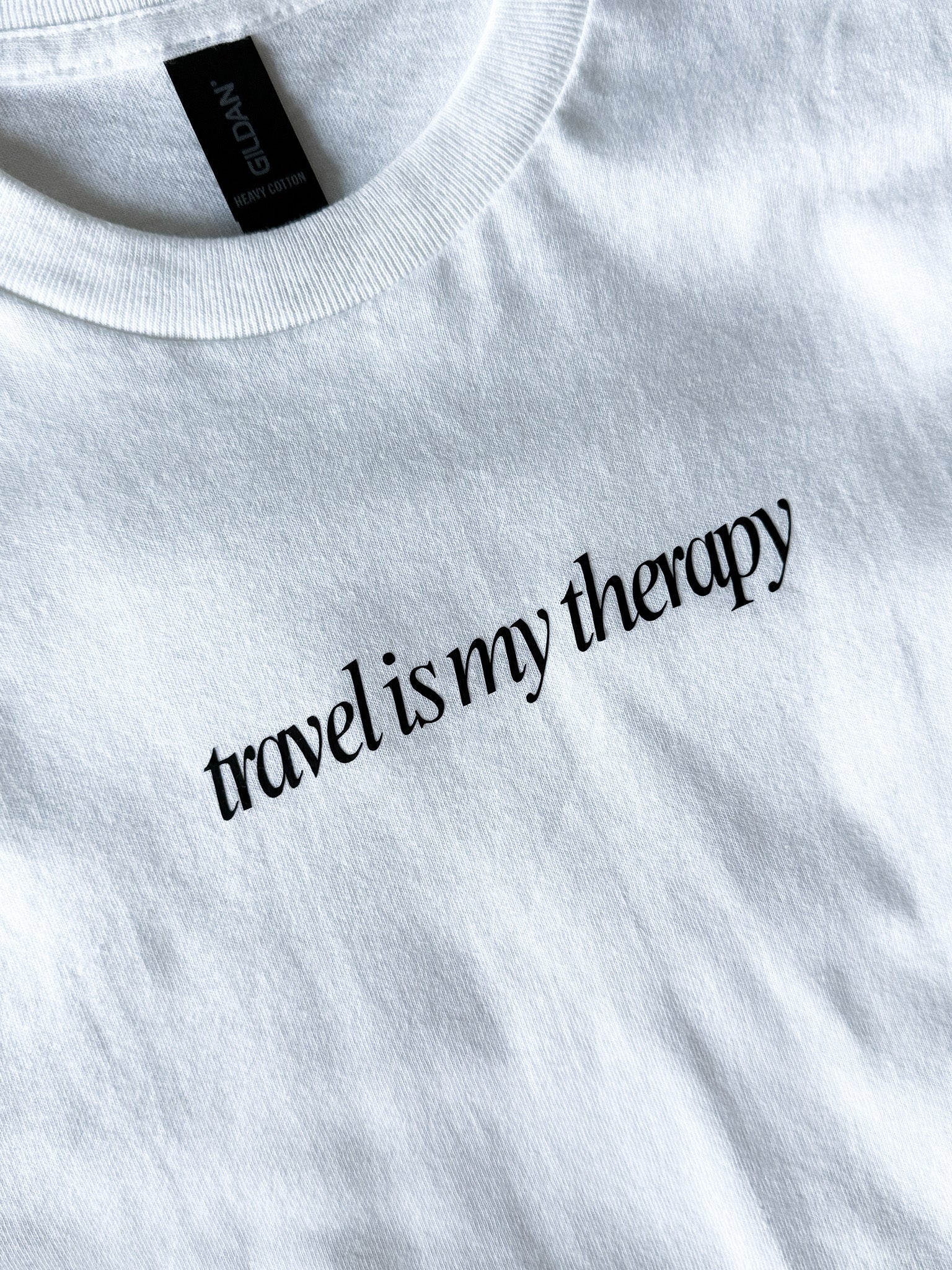 White sweatshirt with 'travel is my therapy' text on a plain background