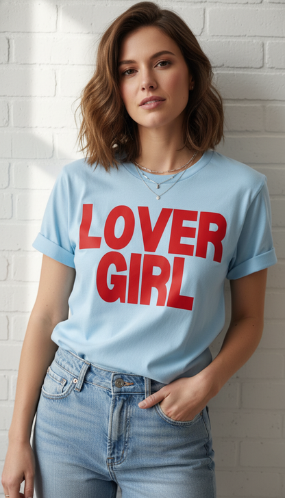 Woman wearing a light blue t-shirt with 'LOVER GIRL' in red text against a white brick wall.